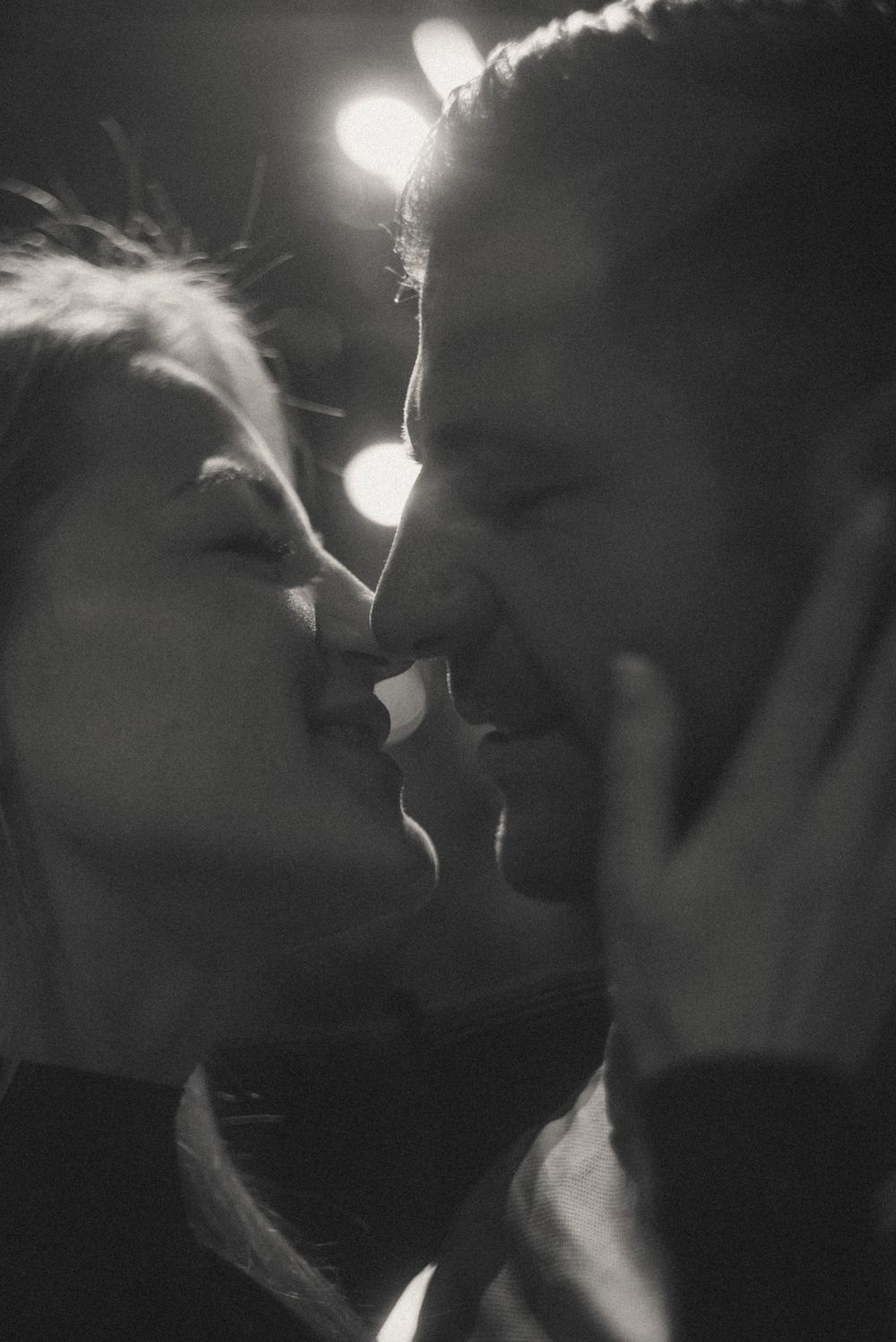 Intimate black and white portrait of a couple sharing a tender moment under dramatic lighting.