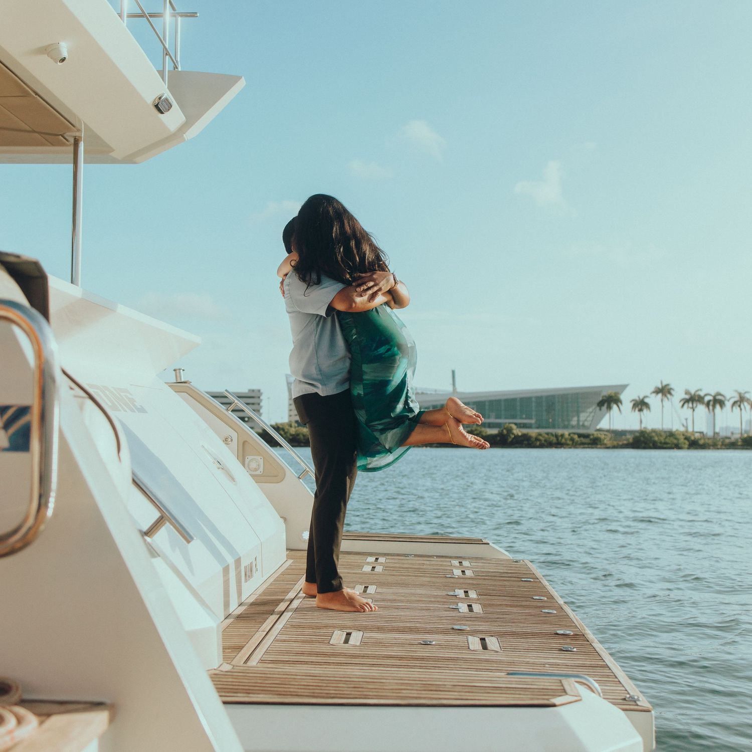 Couple embracing on yacht deck with ocean and palm trees in background.