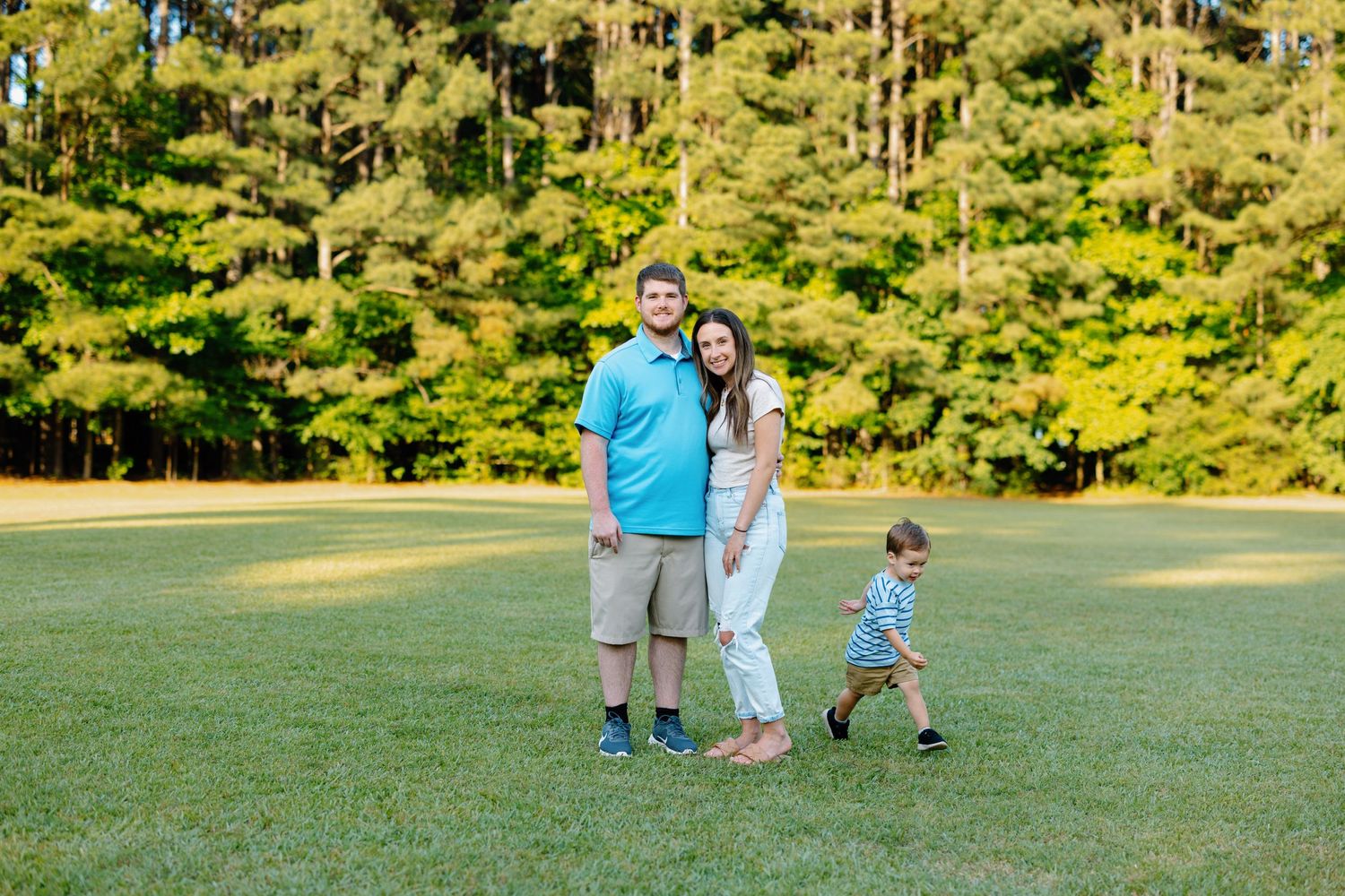 Family enjoying time together on grassy field with pine trees in background.