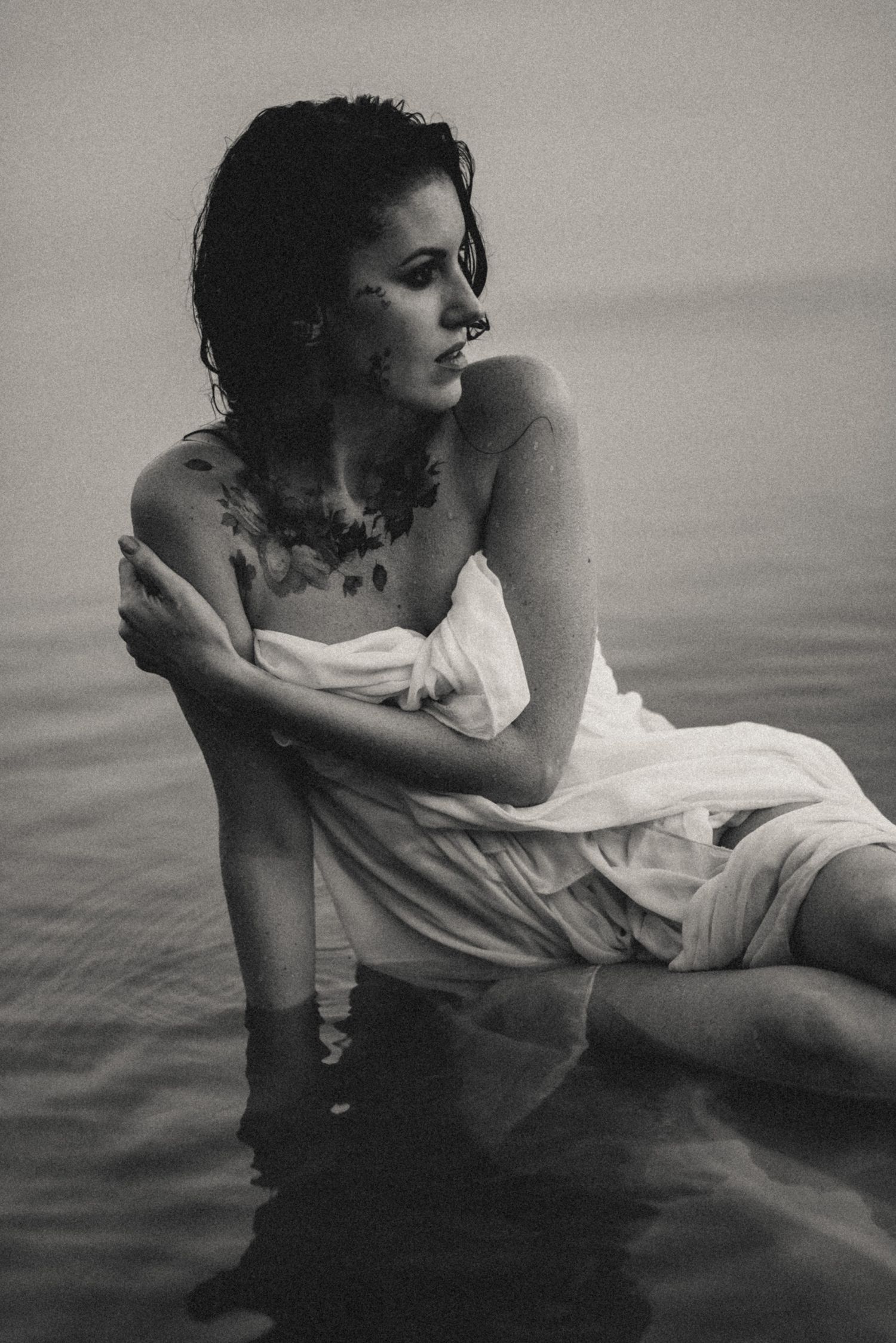 Black and white artistic portrait of a woman in white dress near water.