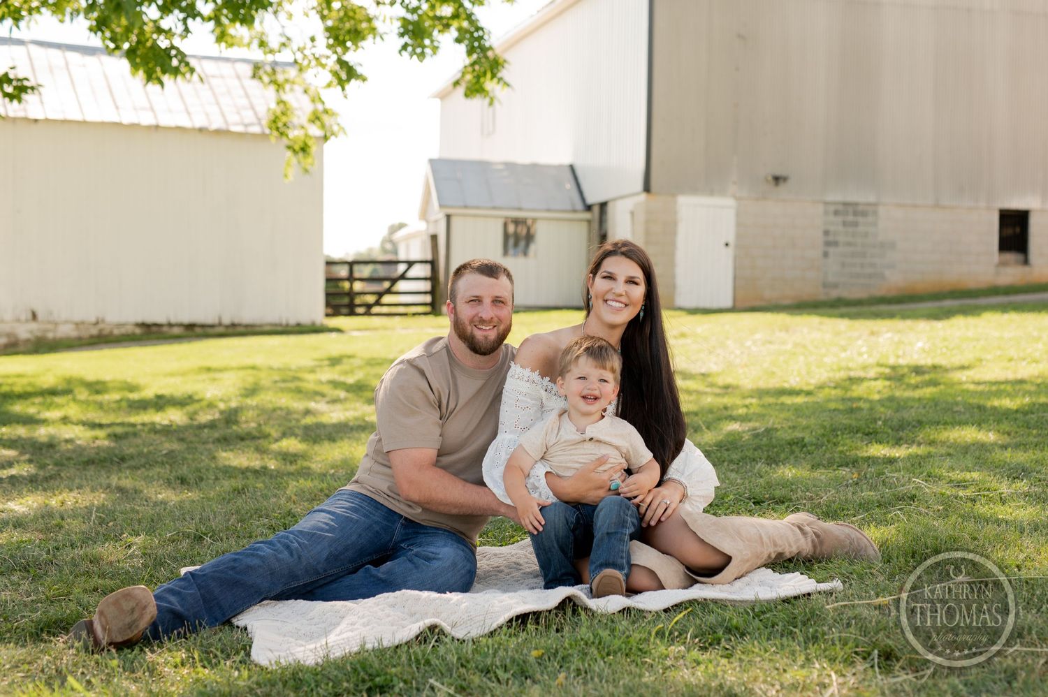Family sitting on blanket for outdoor portrait near white barn.
