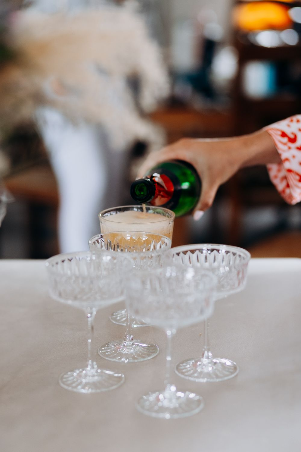 Champagne being poured into elegant crystal coupe glasses on a white surface in a restaurant setting.