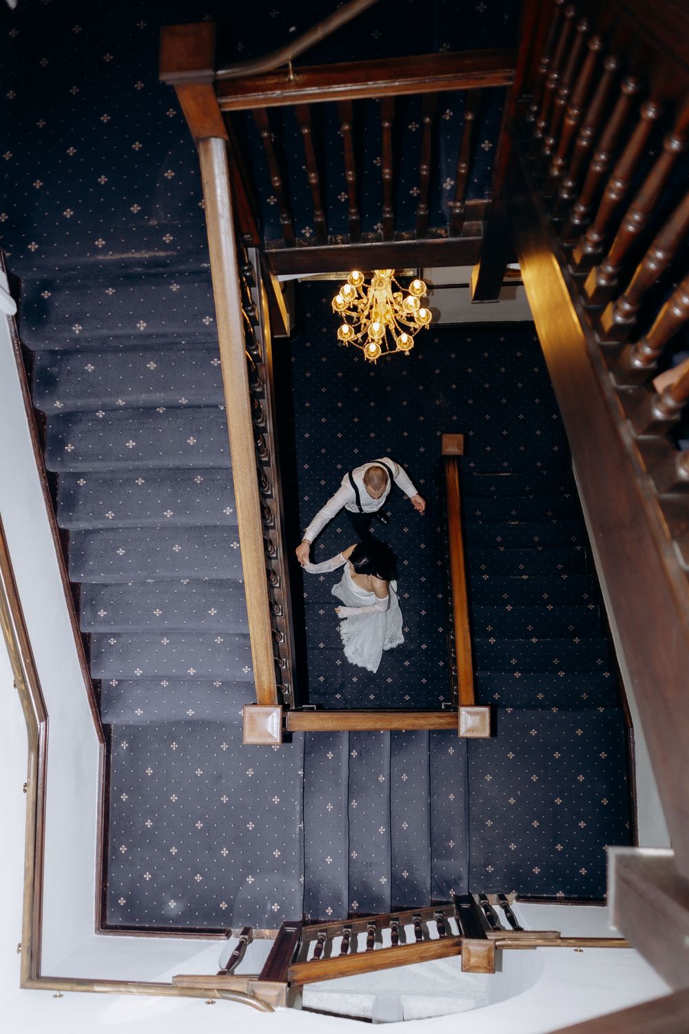 Five sequential photos show a mirror on a dark polka-dotted wall tilting and falling in a hallway with a chandelier.