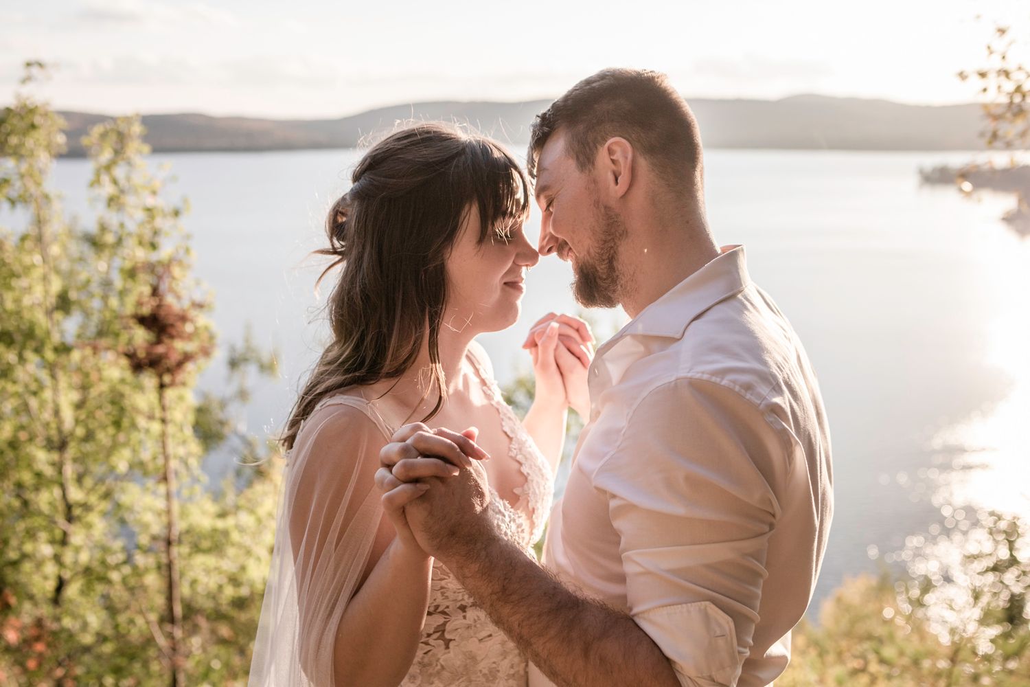 Eloping couple clasp hands and touch noses with closed eyes. Mountains in background. Mont Tremblant, Quebec, Canada.