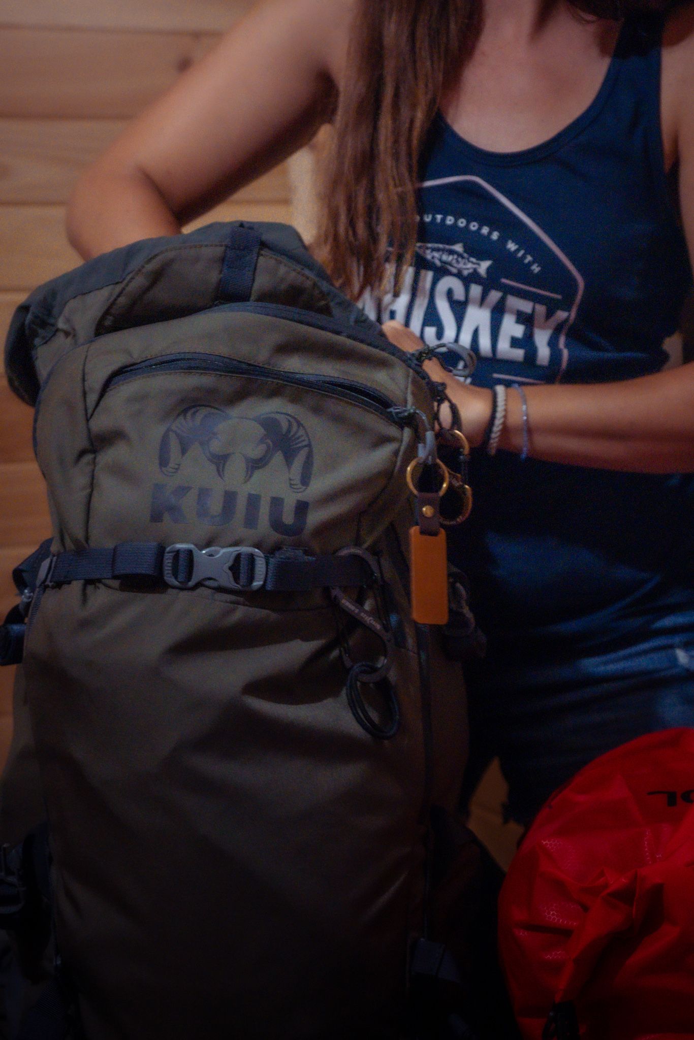Gray outdoor backpack with straps shown against a person wearing a blue tank top in an indoor setting.