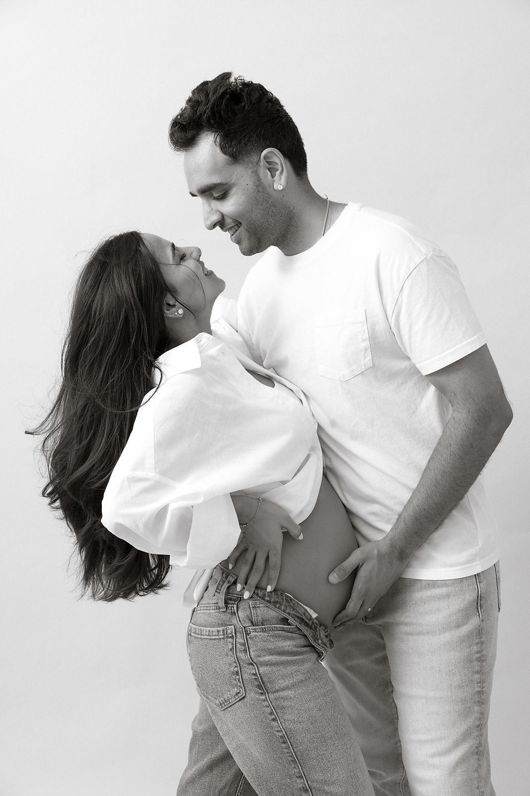 A serene maternity moment by a bright window in winter, wearing a cozy white sweater dress against natural light.