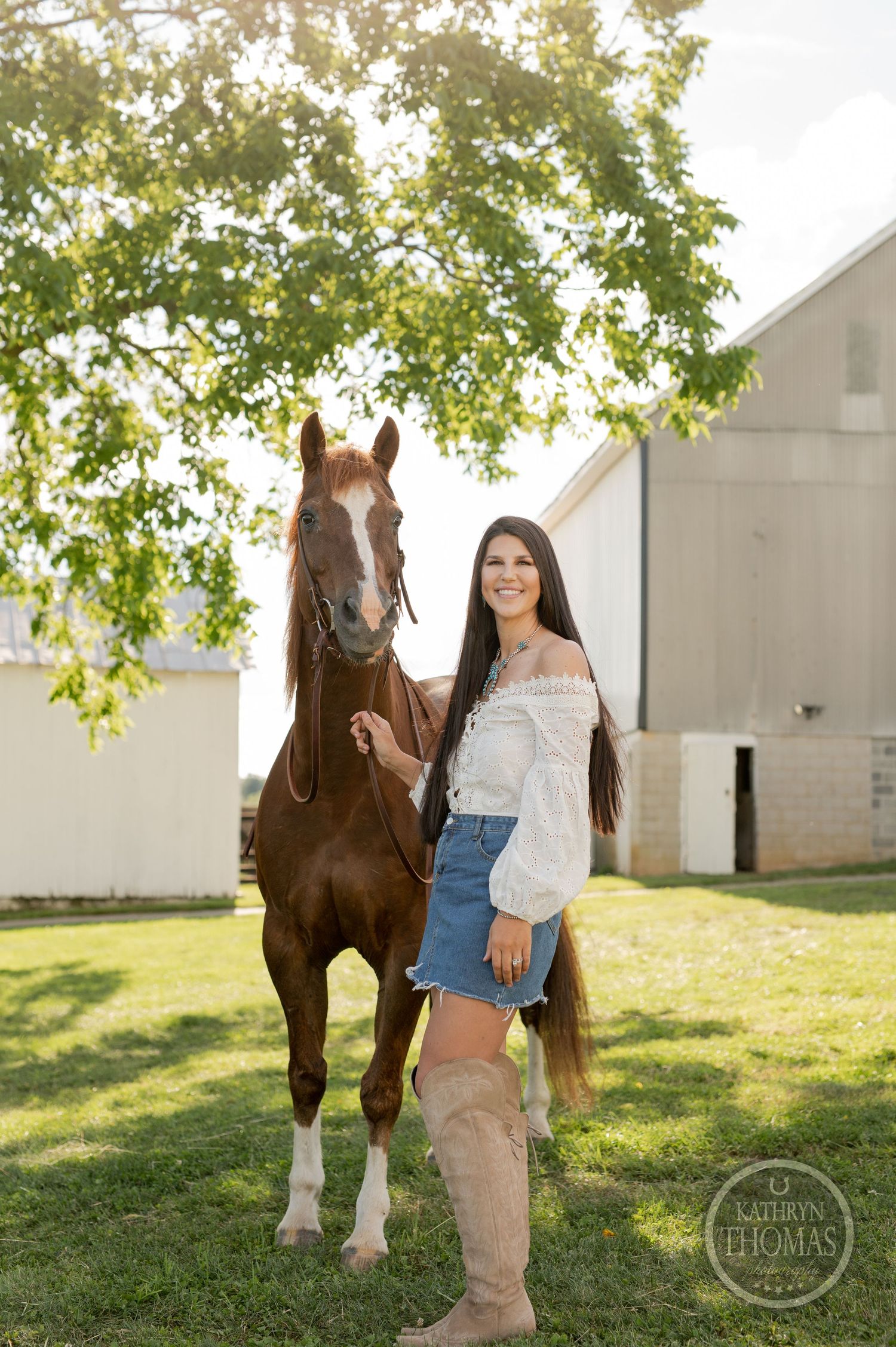 A beautiful brown horse poses with someone in a white peasant top and denim skirt on a sunny farm day.