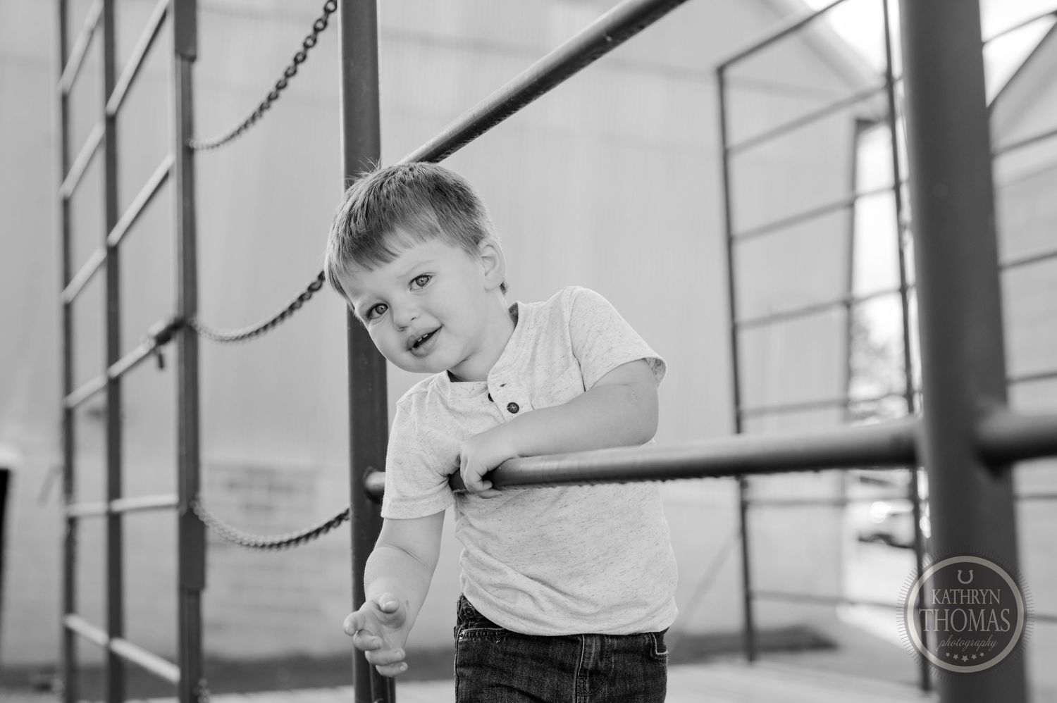Child in polo shirt leans on metal railing in monochrome outdoor setting.