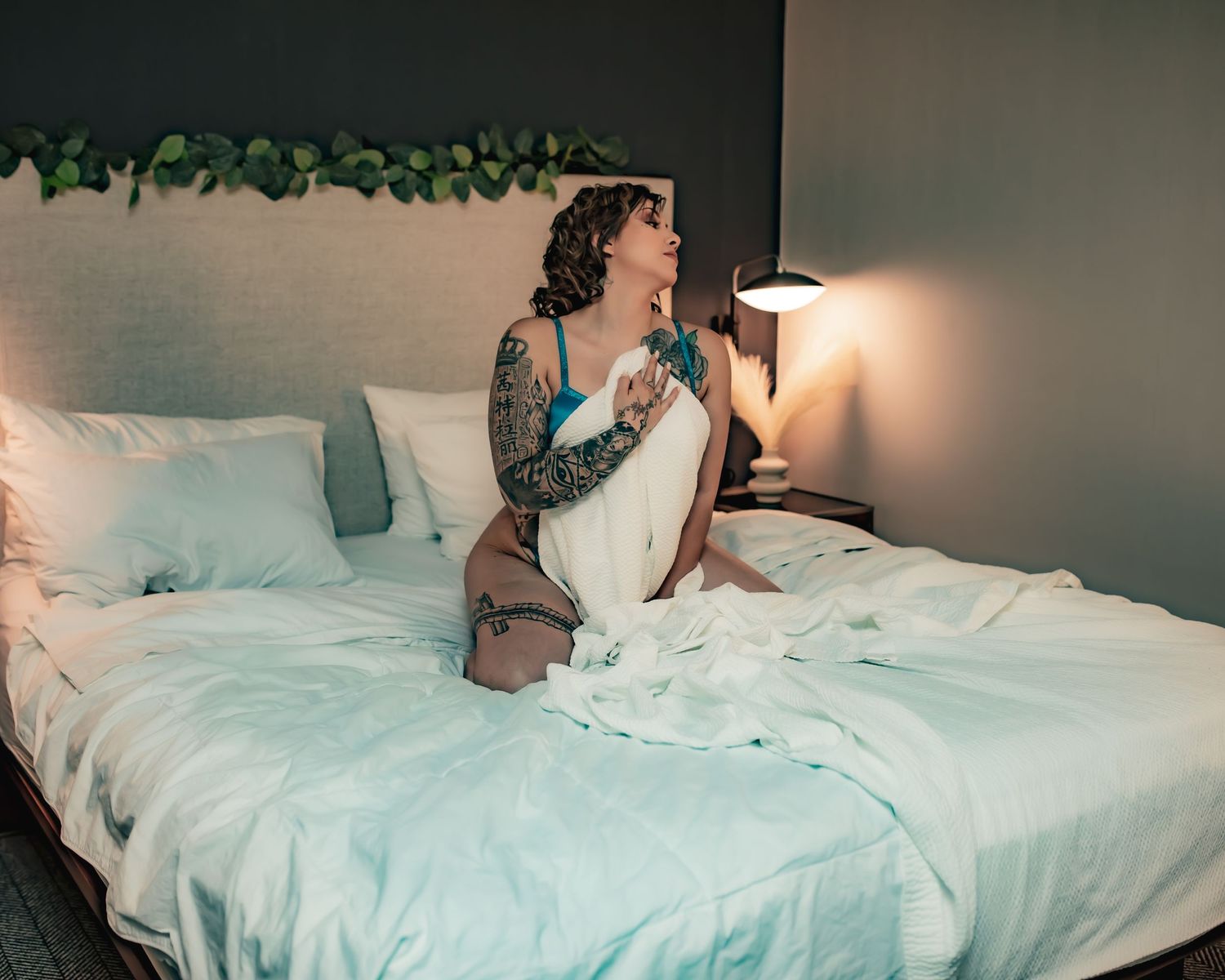 Artistic boudoir portrait on white bedding with decorative vine backdrop.