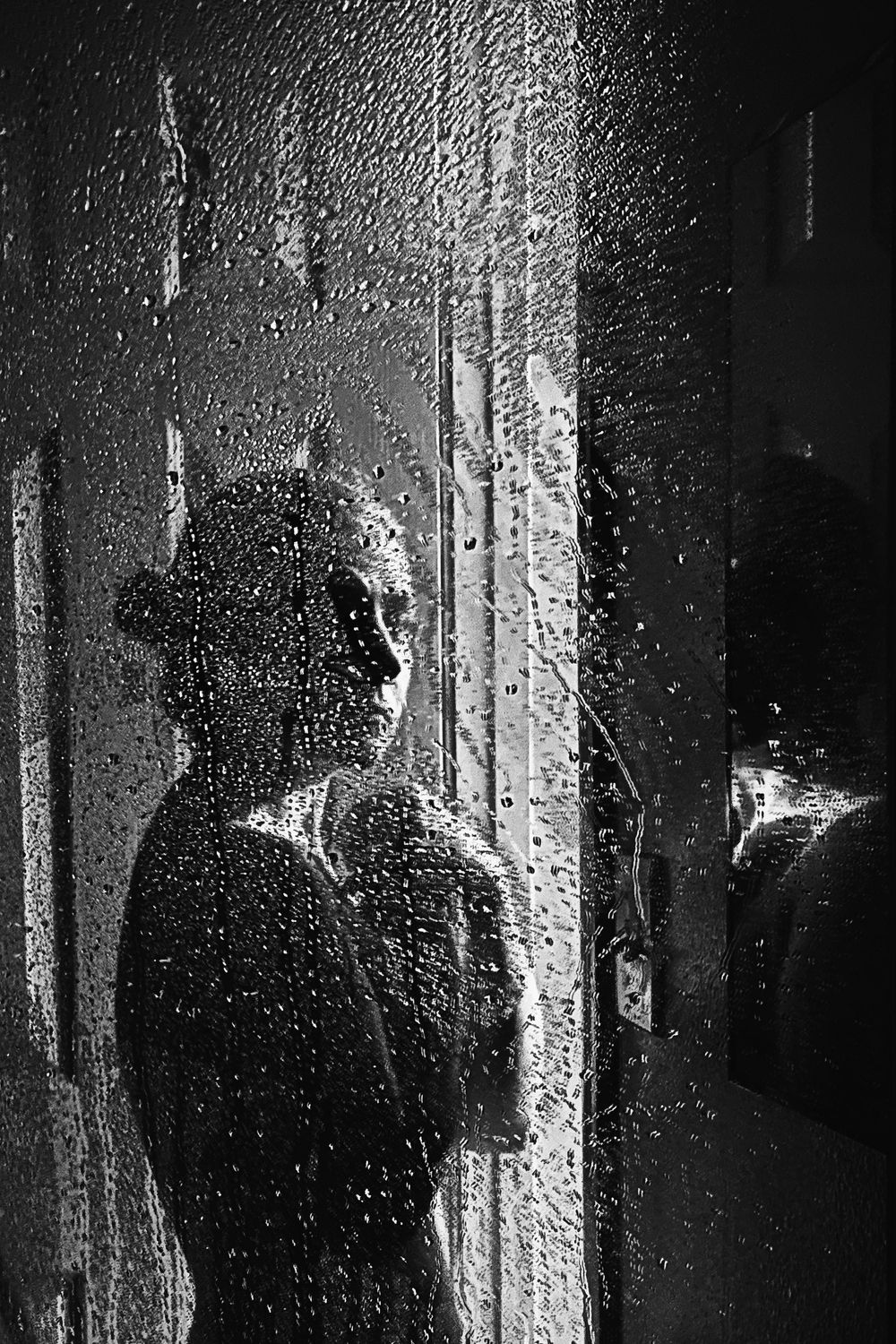 Moody black and white fine art portrait with silhouette behind rain-covered glass