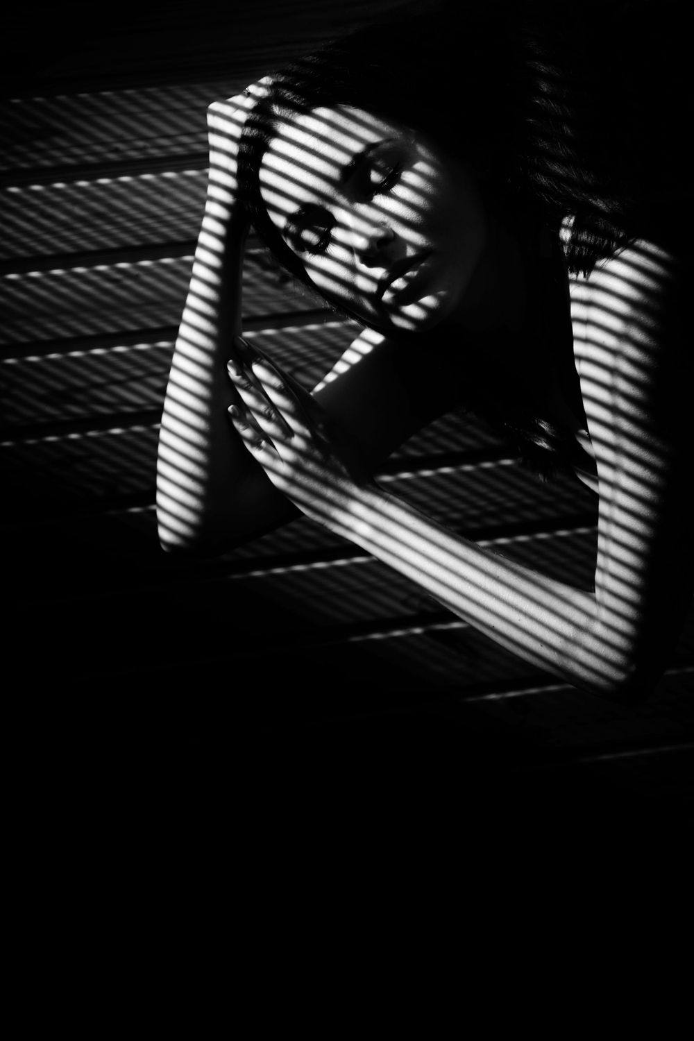Black and white fine art portrait with dramatic light and shadow through blinds