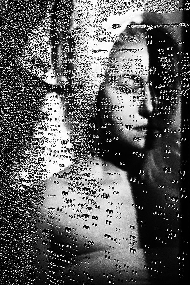 Conceptual black and white fine art portrait of a woman behind wet glass