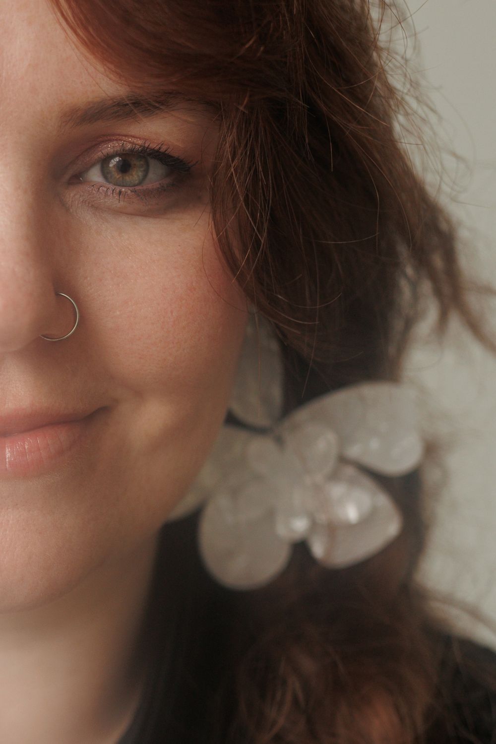 Portrait with messy brown hair and delicate white floral earring against neutral background.