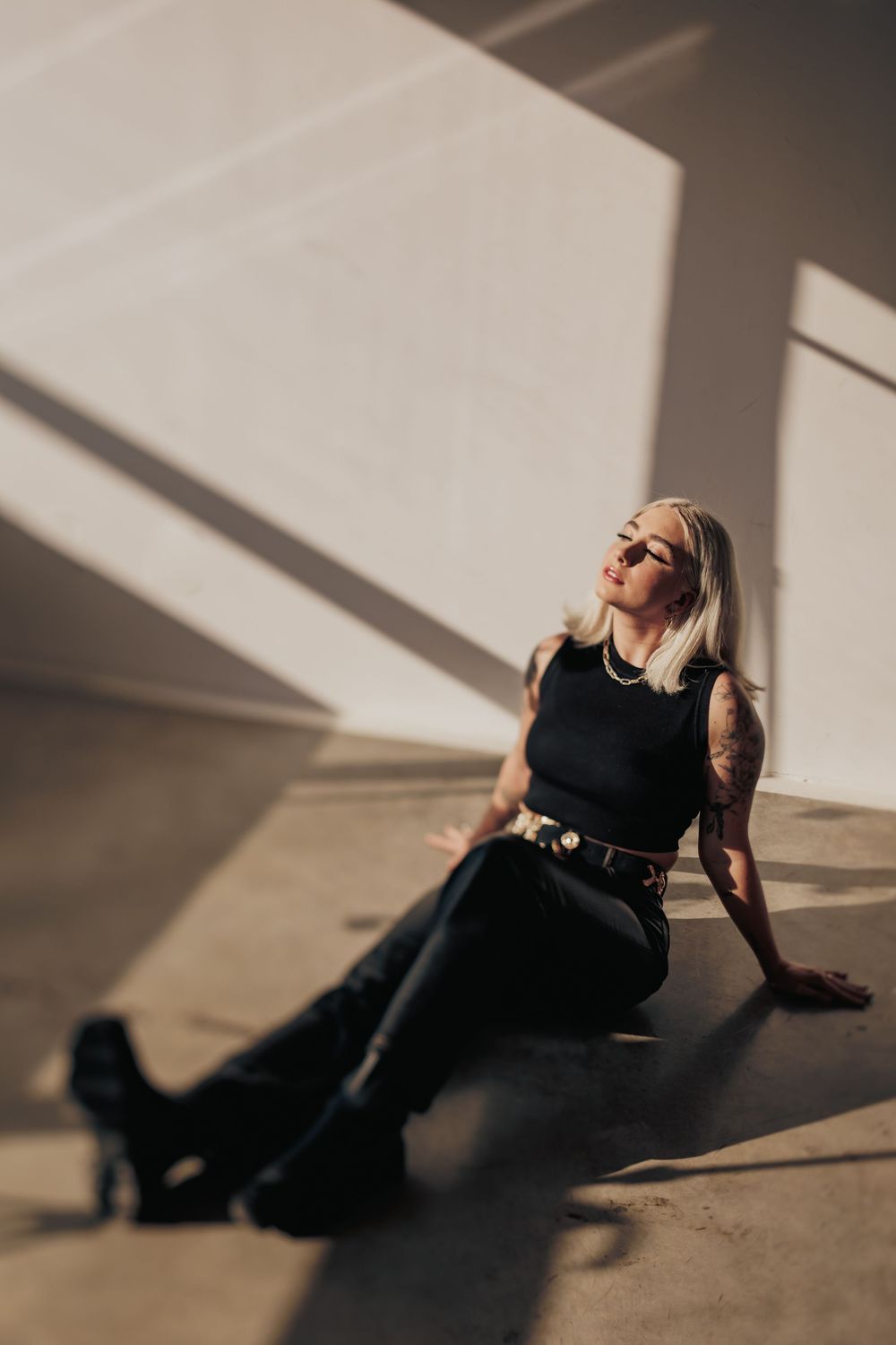 A figure in black dress lies on floor as dramatic shadows from sunlight create artistic patterns on the ground.