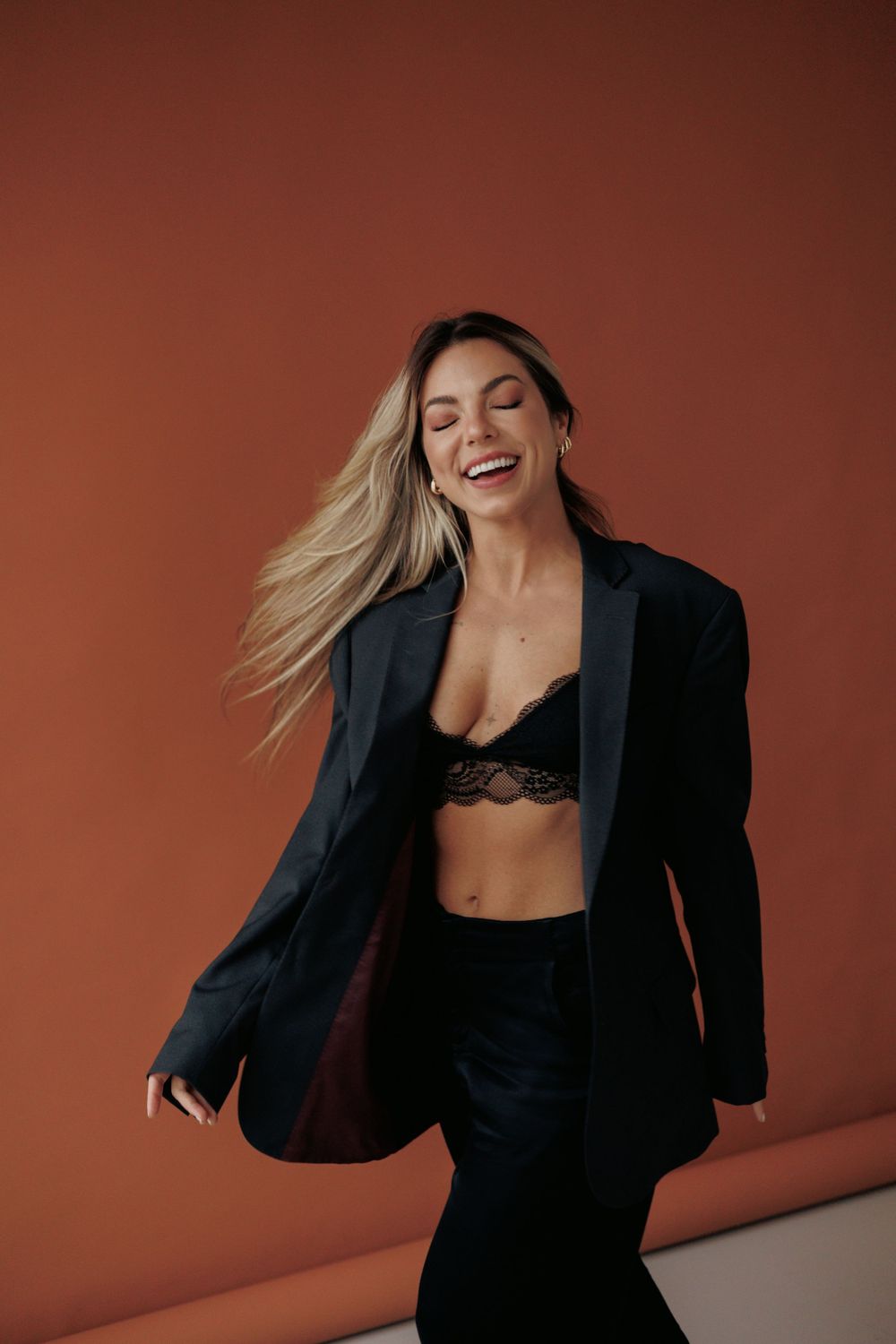 Someone wearing a black blazer and bralette poses confidently against an orange background.