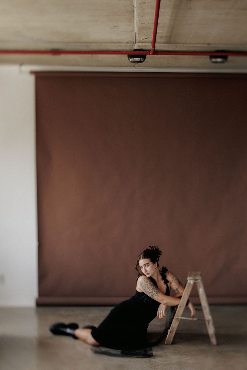A figure in black clothing performs a graceful floor dance sequence in an empty studio space.