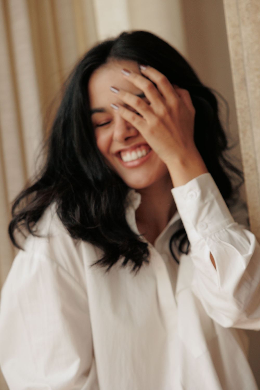 Candid portrait of woman laughing in white button-down shirt against neutral background.