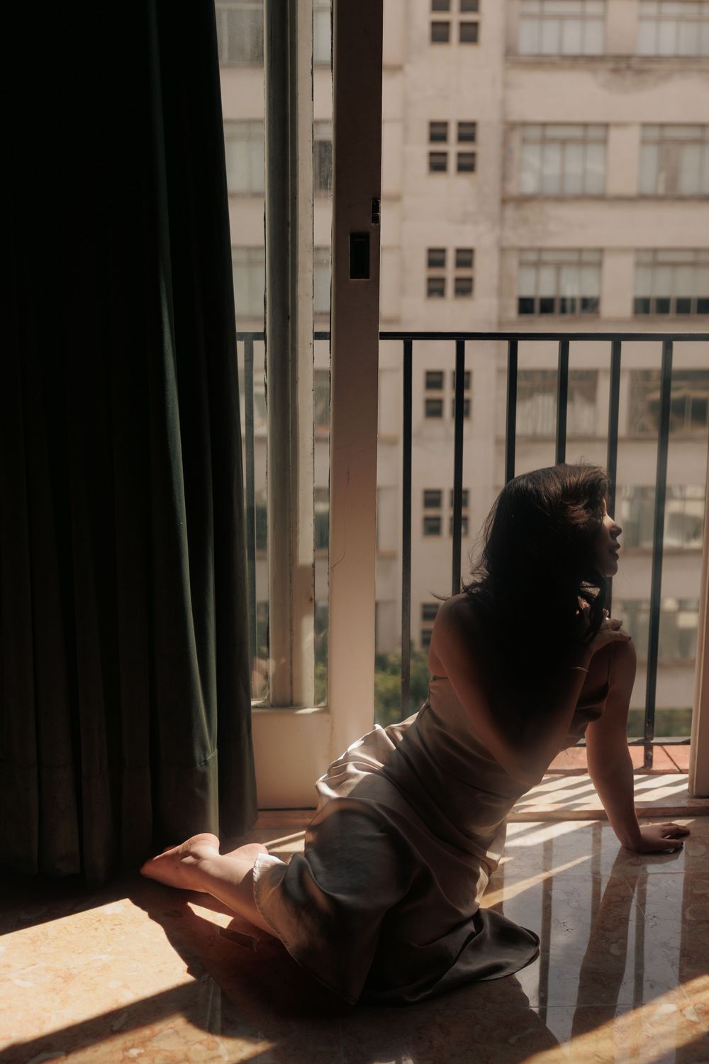 Silhouette sits by large window with sunlight streaming in and city buildings visible in background.