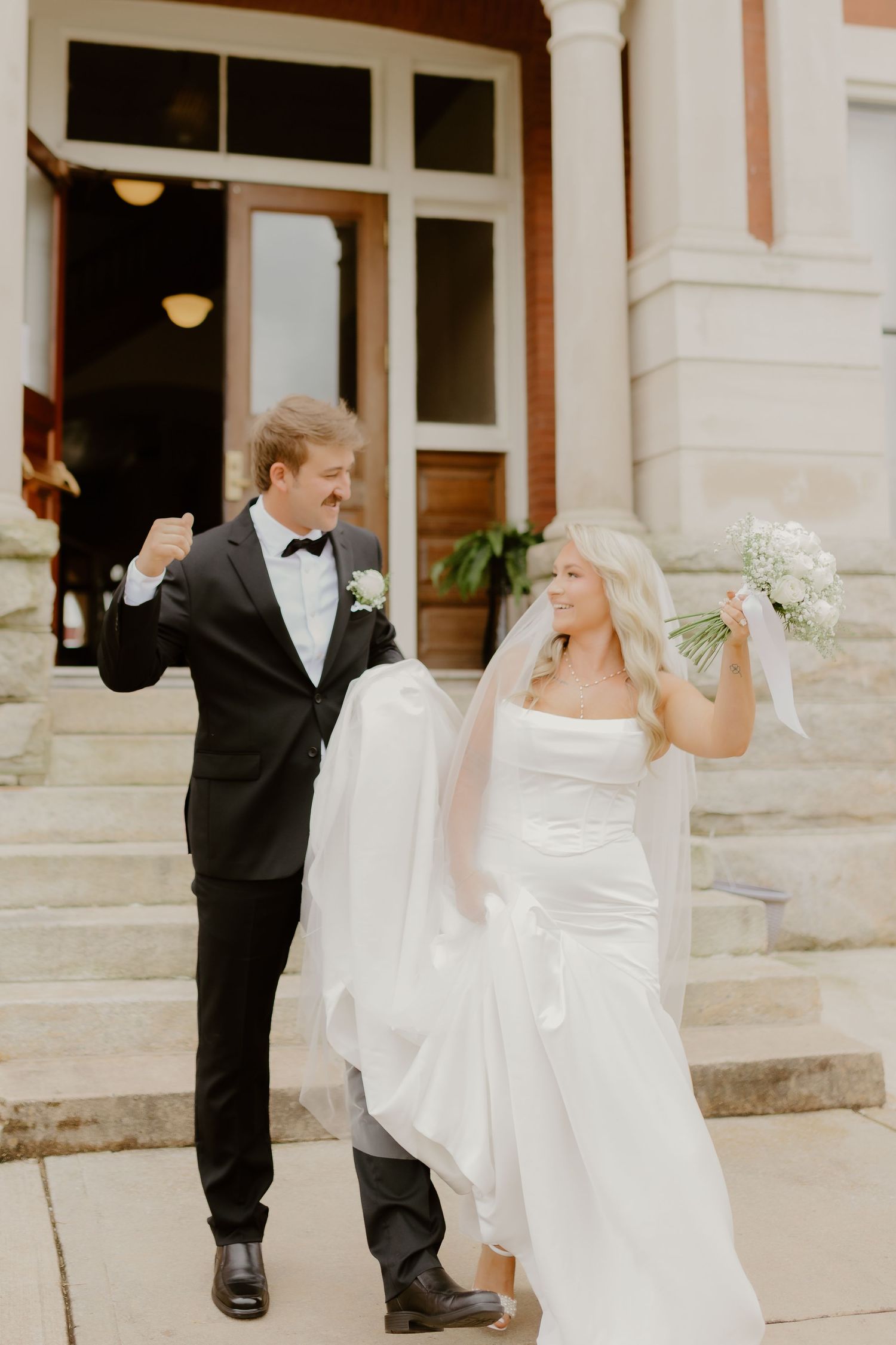 Romantic wedding couple embraces on a sunlit dirt path surrounded by lush green trees in an outdoor setting.