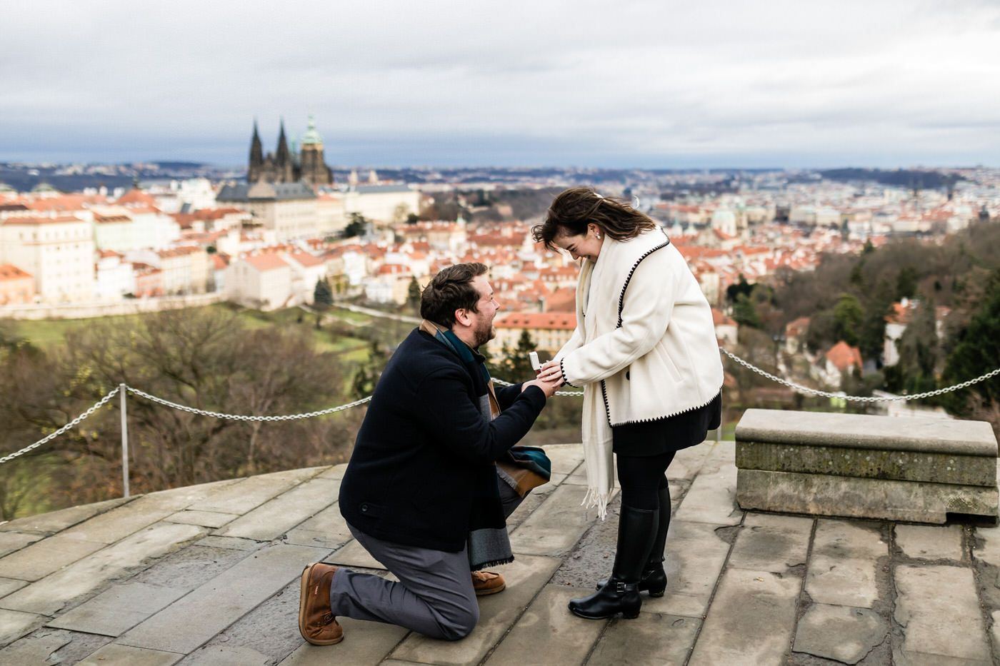 A romantic proposal moment at a scenic overlook with Prague Castle and the city skyline in the background.