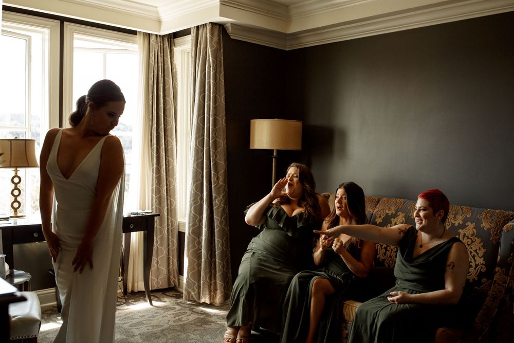 An elegant wedding dress is shown while others sit on a couch in a dimly lit room.
