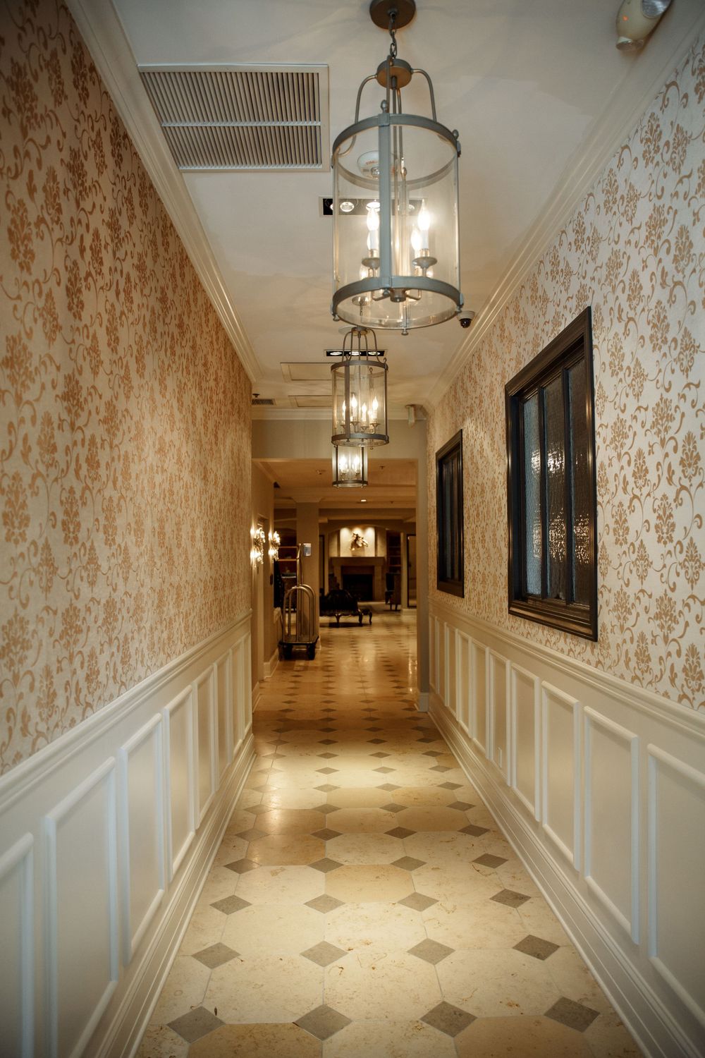 Luxurious hotel hallway with patterned wallpaper, wainscoting and pendant lighting.