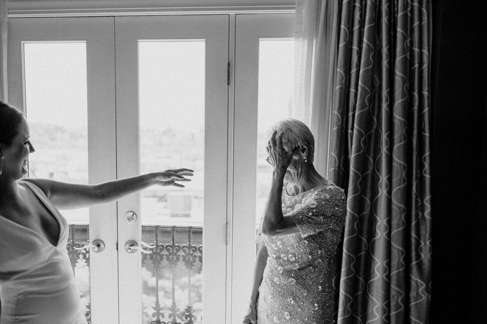 Two figures interact near French doors in an emotional black and white wedding moment.