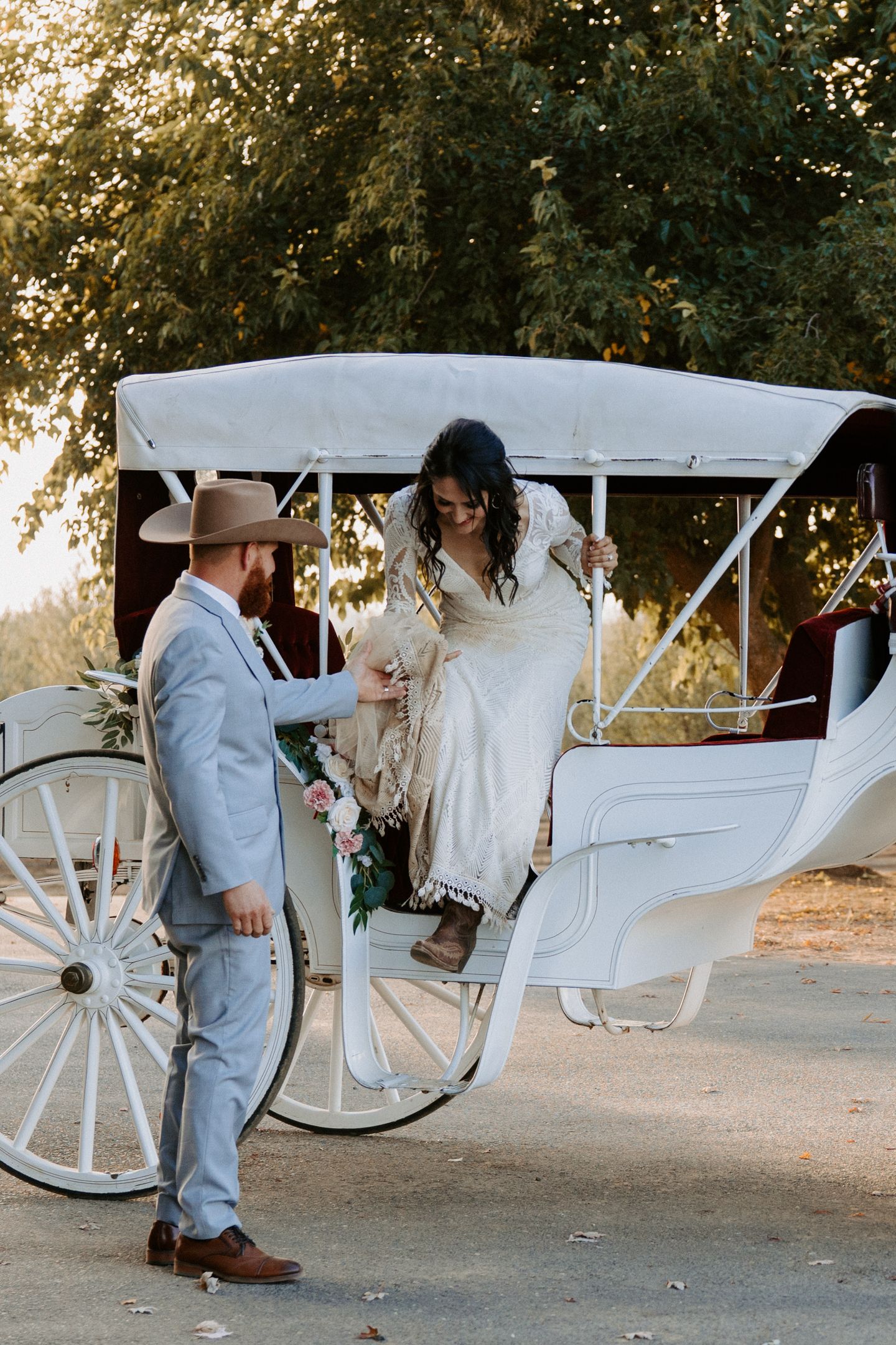 A groom helps his bride out of a horse-drawn carriage during the golden hour as a part of their wedding photoshoot.