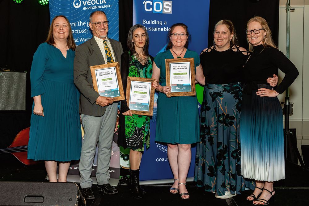 Group of six professionals holding award certificates at a Veolia and COS sustainable building industry awards ceremony.