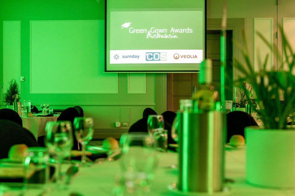 Green Gown Awards ceremony venue with illuminated screen displaying sponsors, elegantly set tables with glassware.