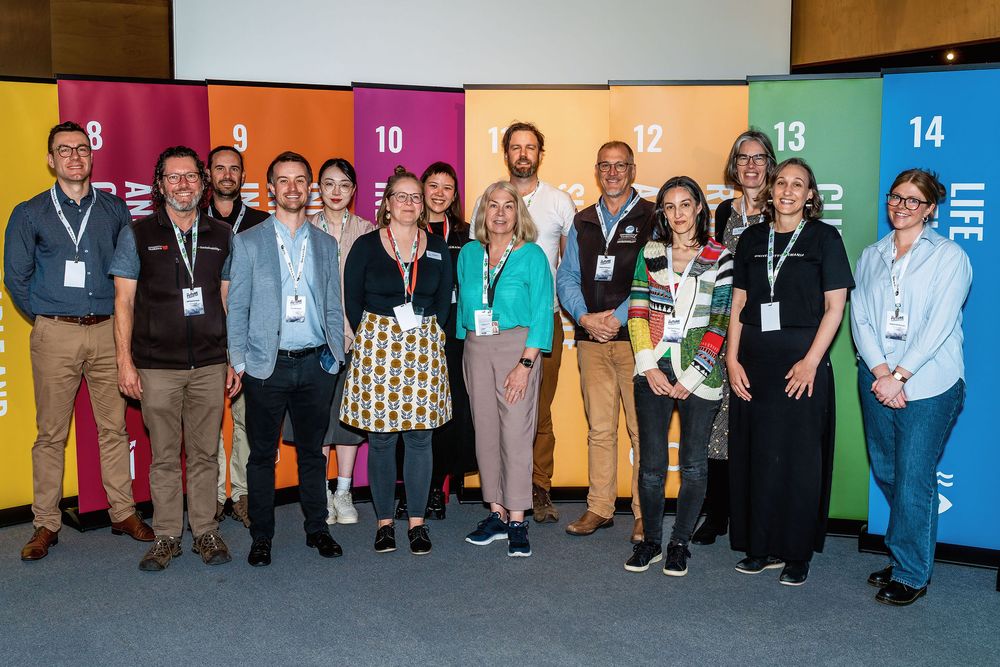 Group of professionals posing together in front of colorful UN Sustainable Development Goals banners at a conference.