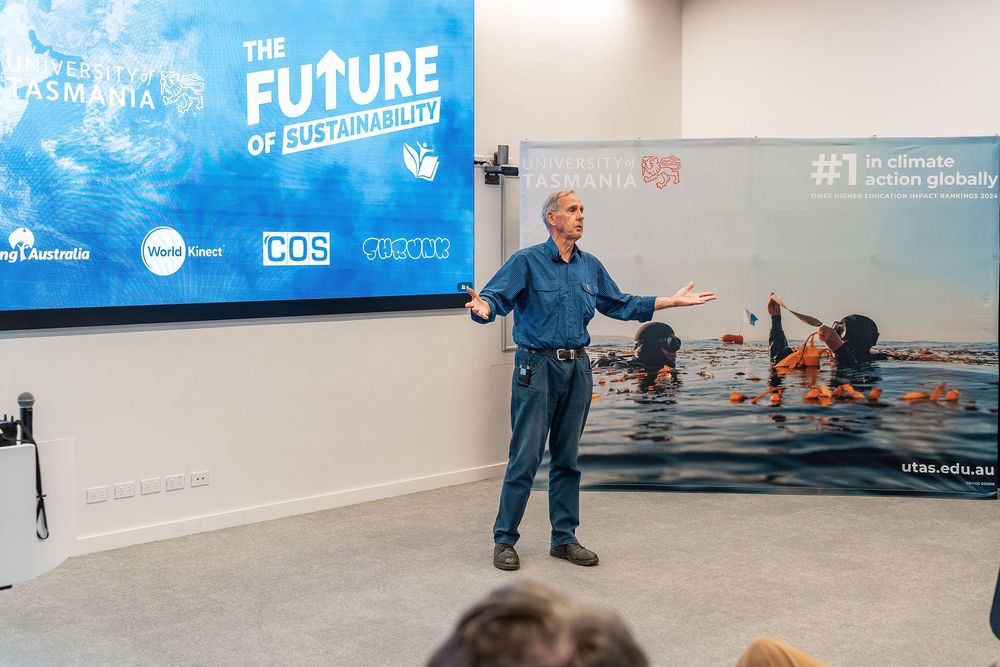 Man presenting at The Future of Sustainability conference with sponsor logos and ocean conservation imagery displayed behind him.