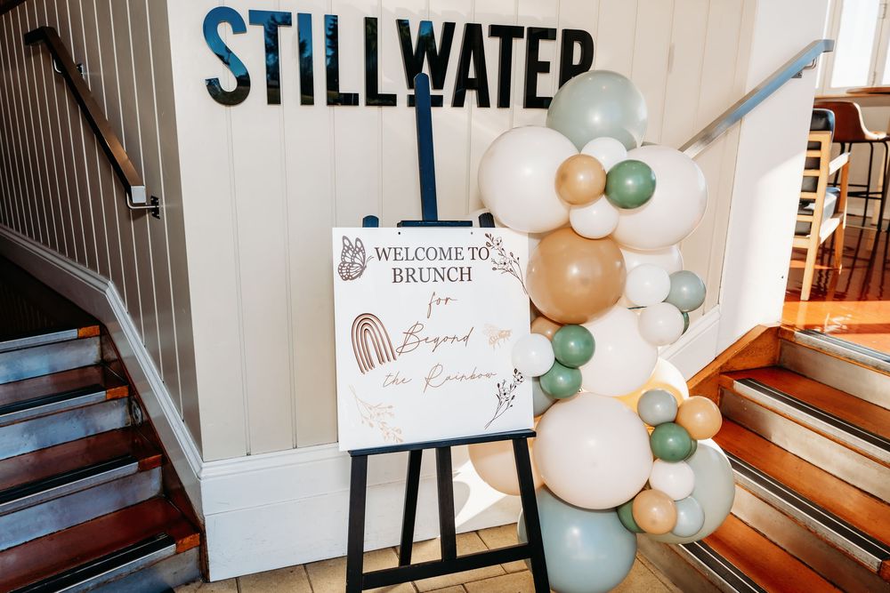 Welcome to Brunch sign on easel with sage green, gold, and white balloon garland at Stillwater venue.