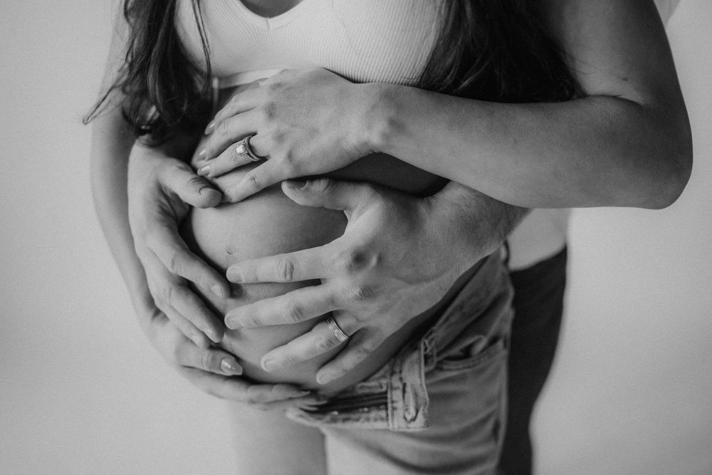 Close-up black and white shot showing hands gently cradling a pregnant belly.