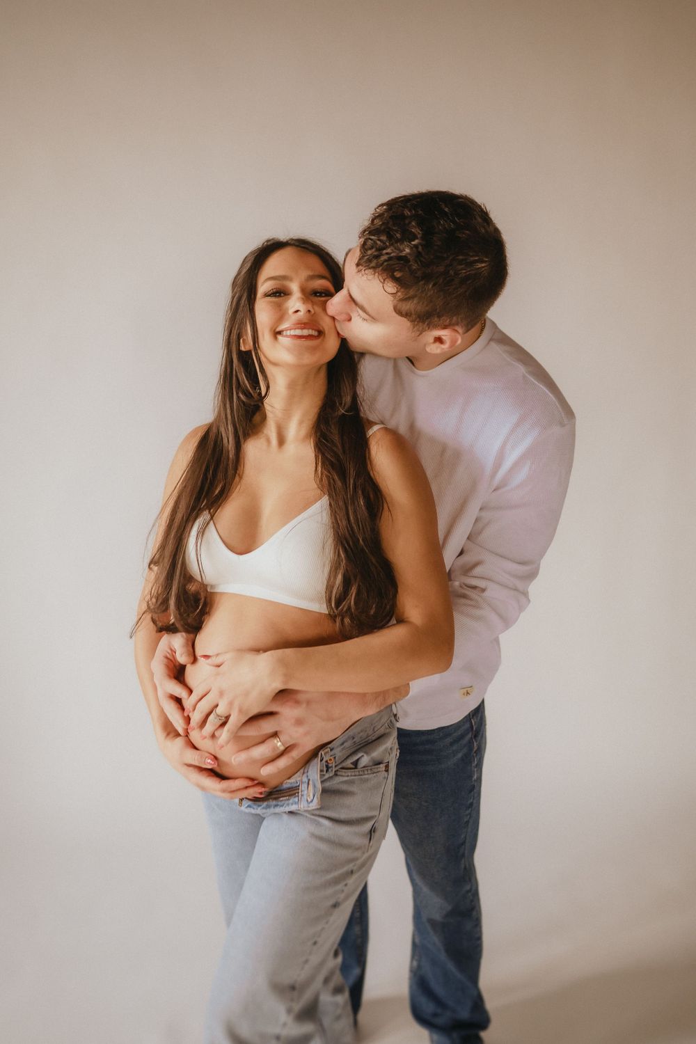 A tender moment between a couple wearing casual attire against a plain white wall.