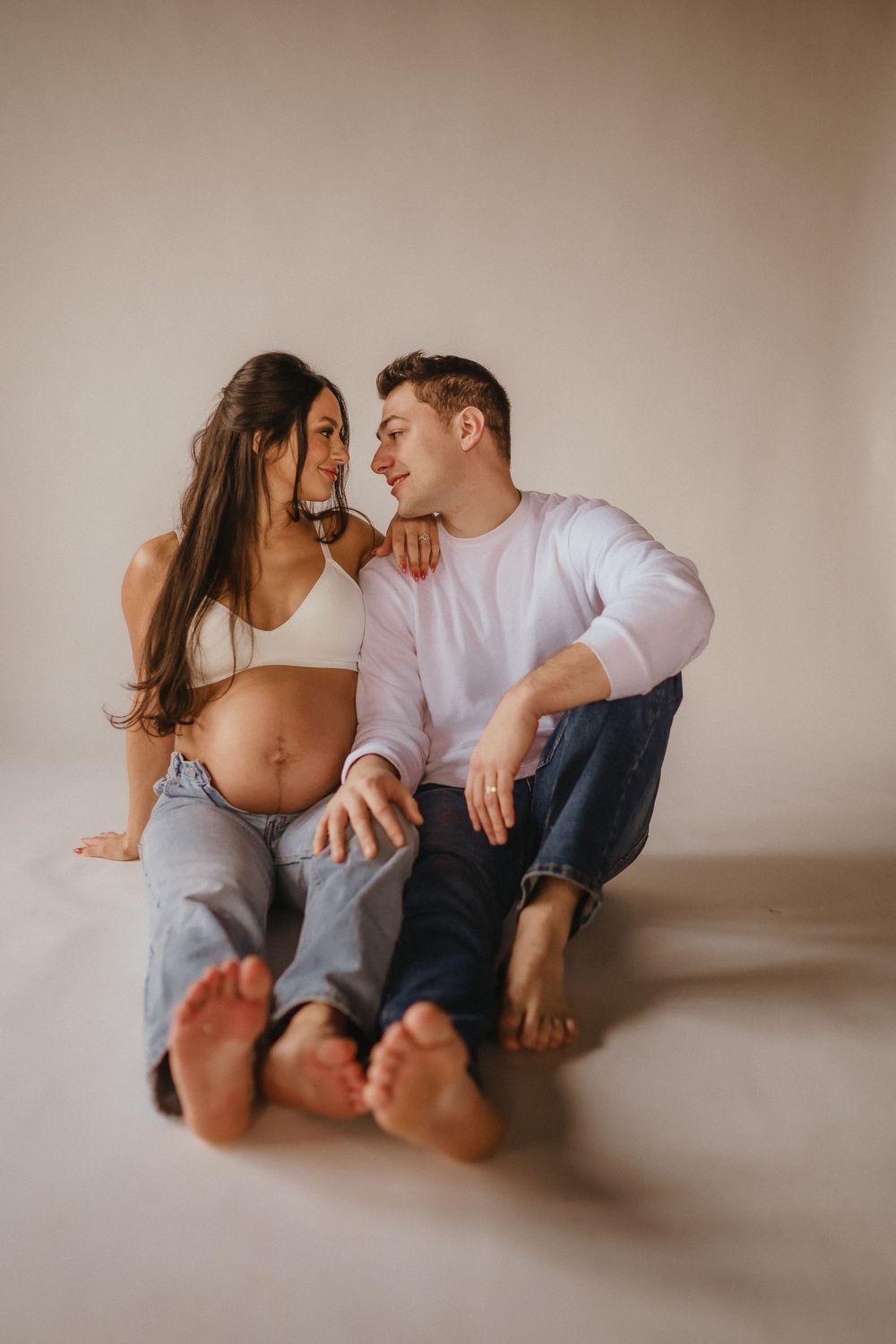 Couple relaxing together on floor during intimate maternity photoshoot with bare feet and natural lighting.