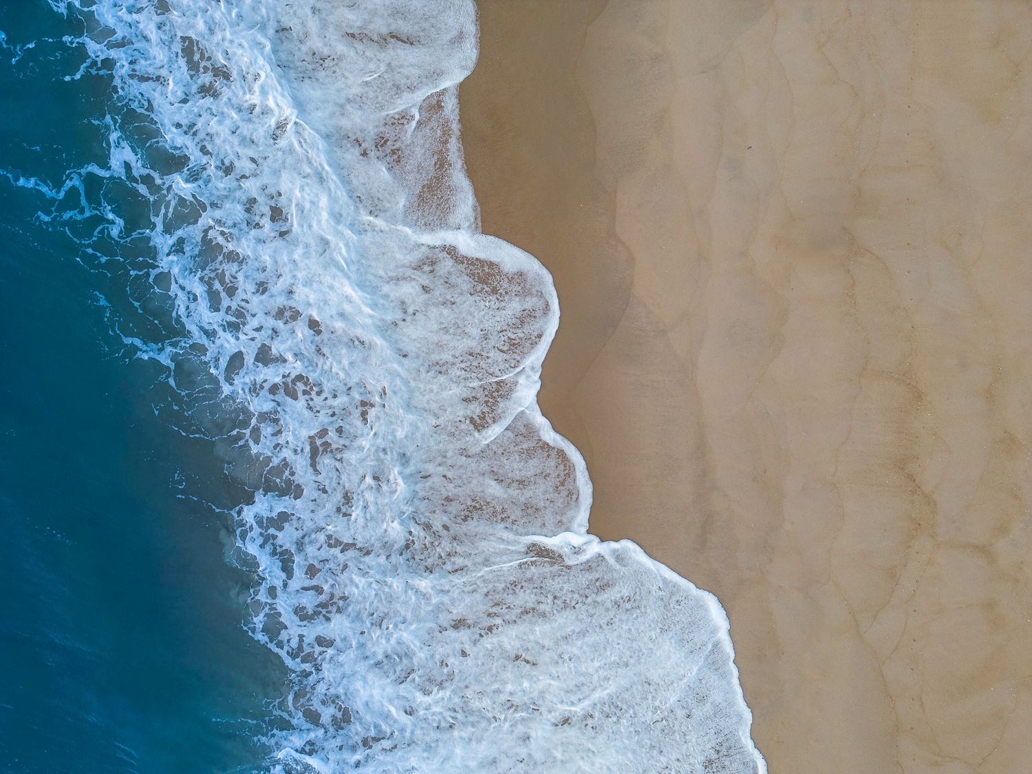 Aerial view of ocean waves meeting sandy beach creating a dramatic curved shoreline pattern from Wrightsville Beach.