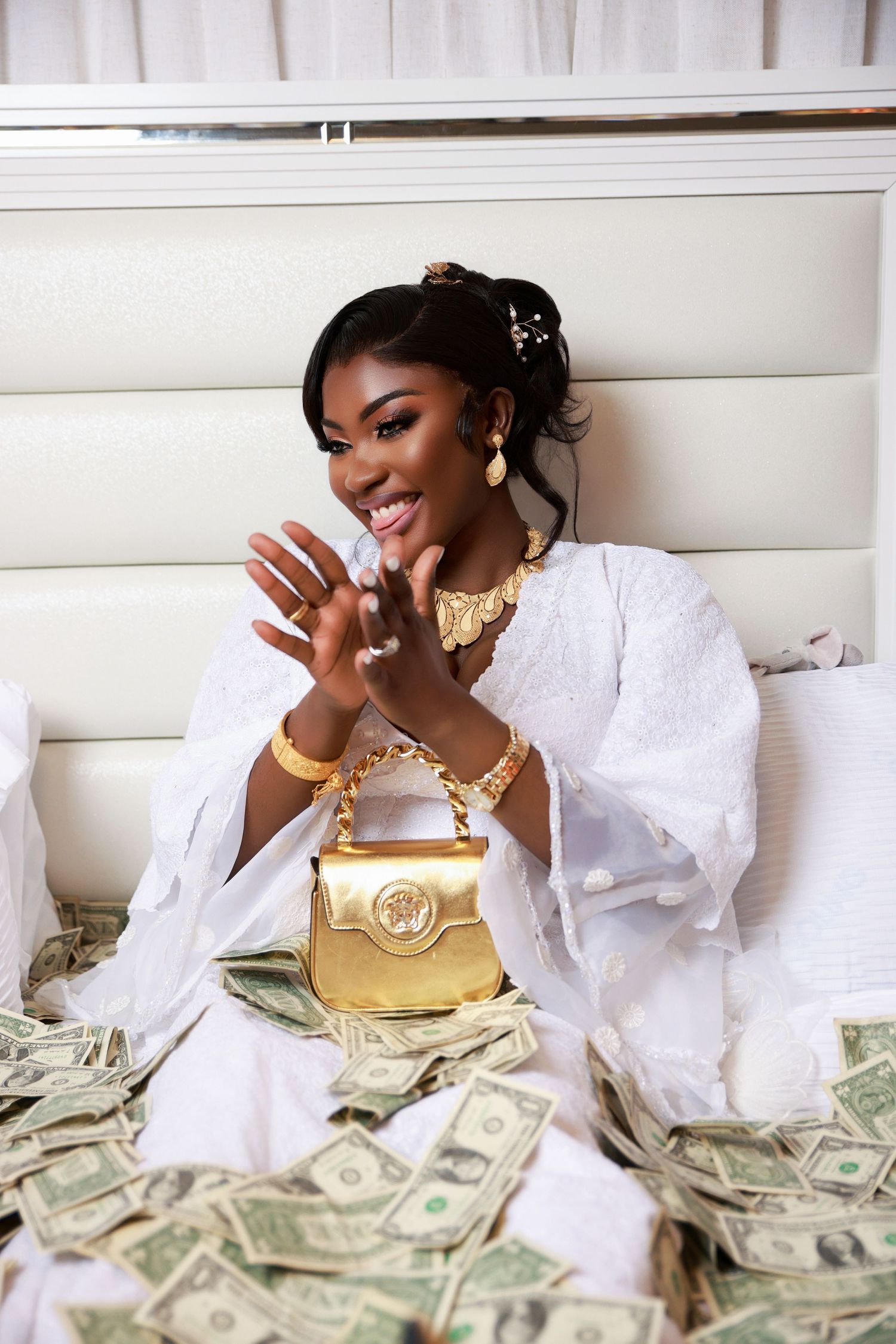 Woman in white outfit laughs while posing with gold purse and money spread around.