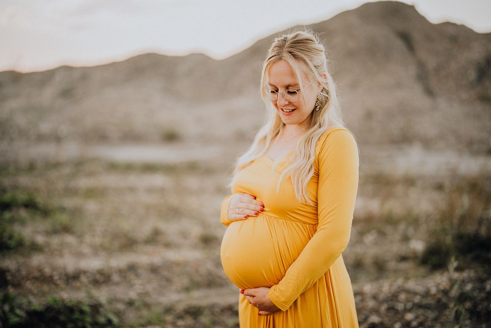 Side view of pregnancy silhouette in marigold dress against desert backdrop.