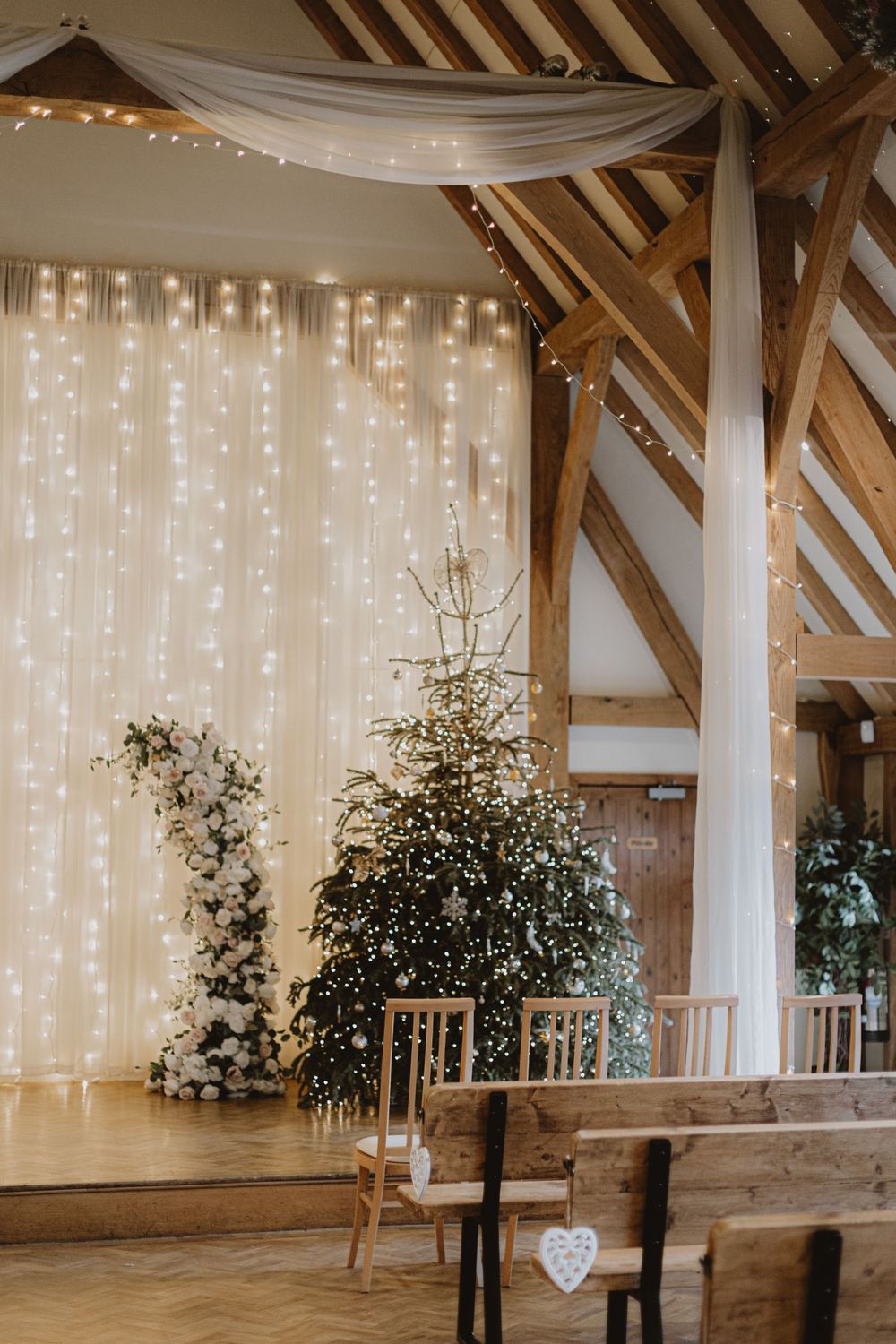 Rustic barn wedding venue with exposed wooden beams and twinkling fairy light curtains.
