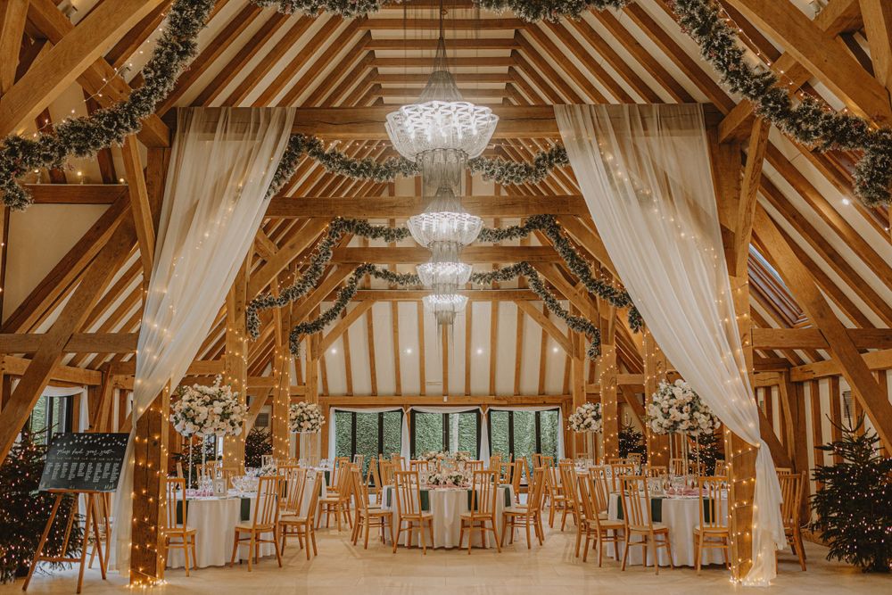 Panoramic view of a decorated barn wedding venue with white draping and chandeliers.