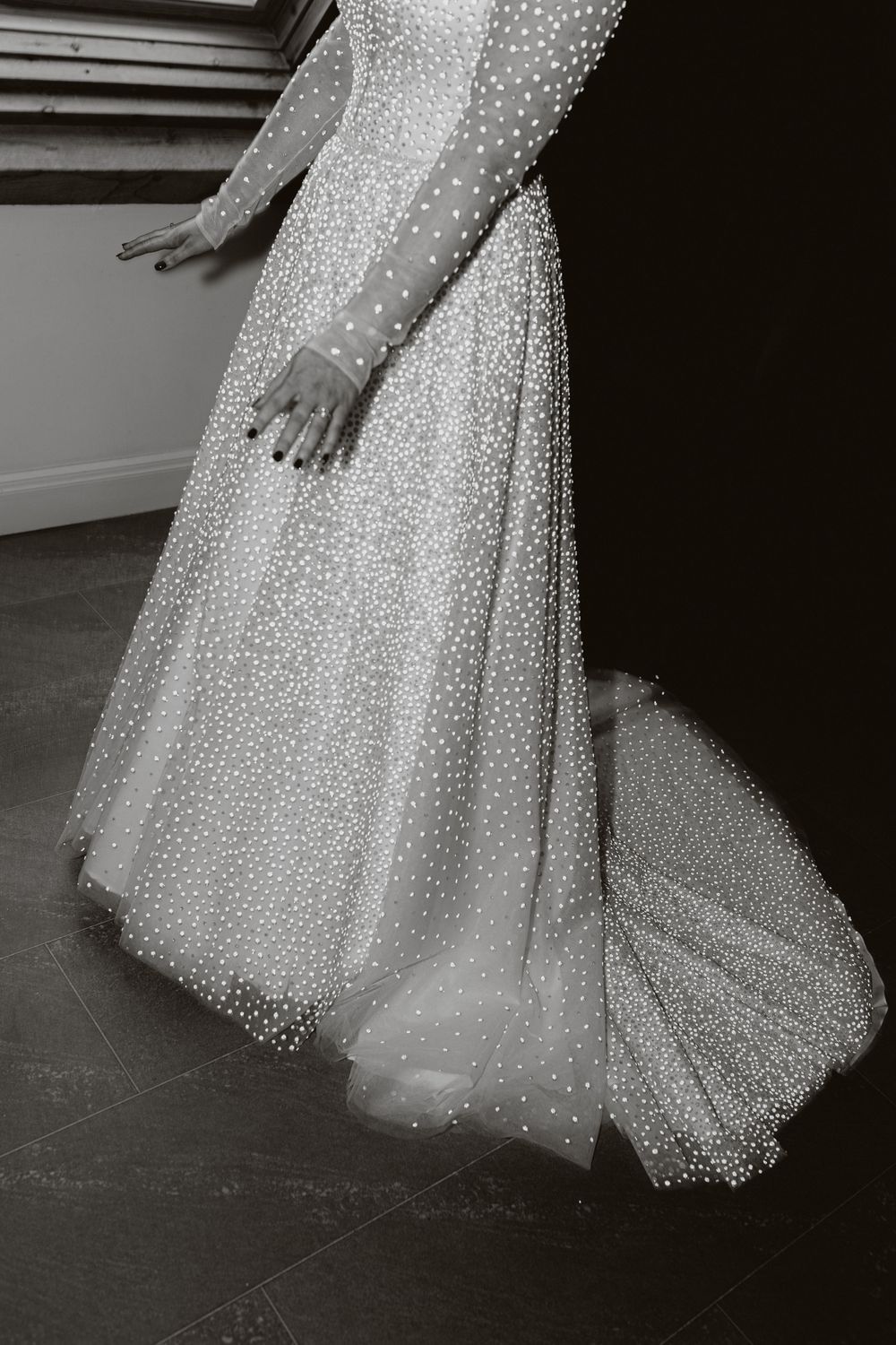 Black and white photo of a pearl-embellished wedding dress train on dark floor.