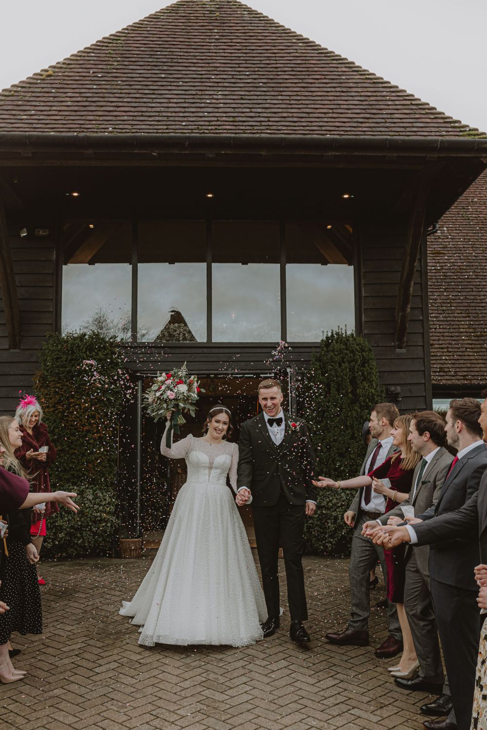 Wedding party gathered outside a modern brick building with paved courtyard.