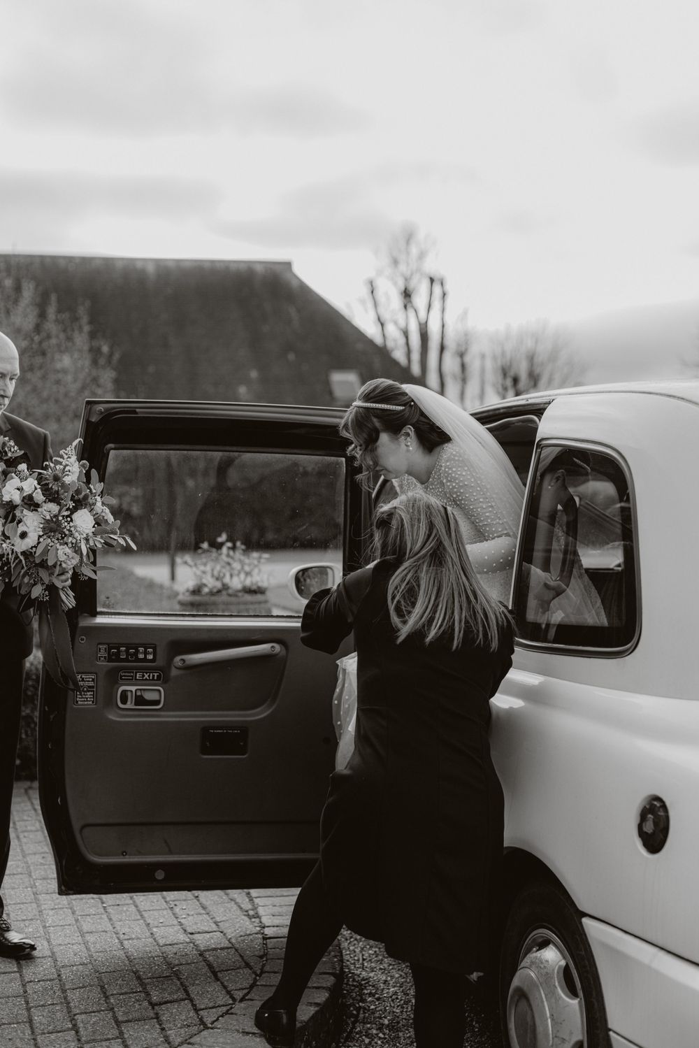 Black and white photo of guests arriving at a wedding in vintage cars.