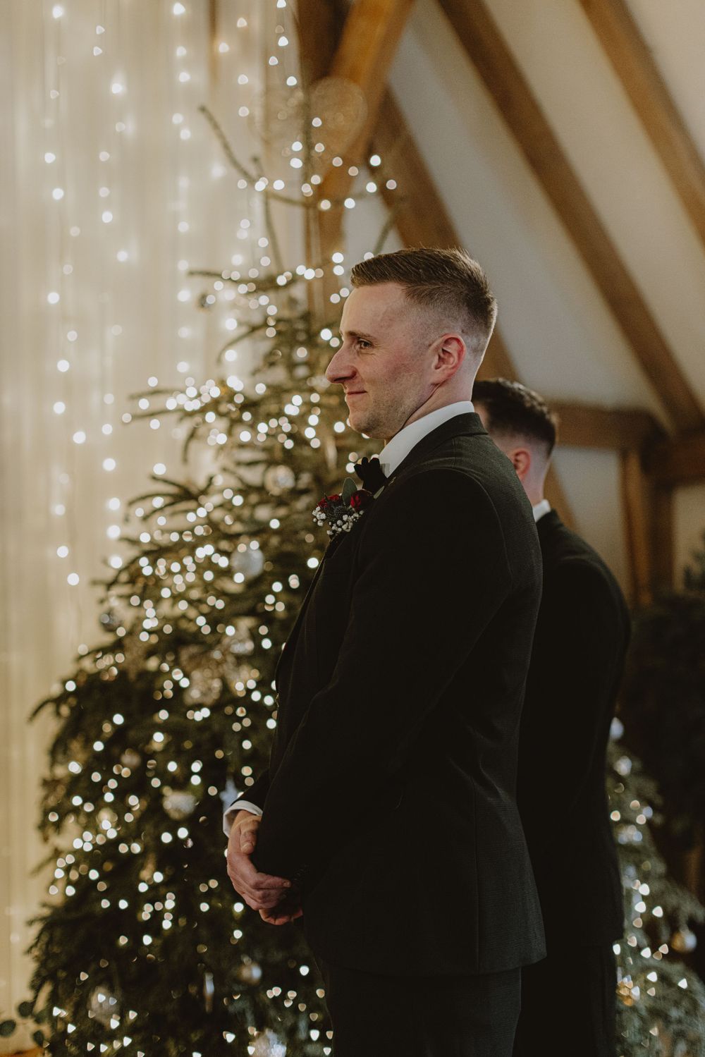 Wedding ceremony setup with decorated Christmas trees and fairy lights in a rustic barn venue.