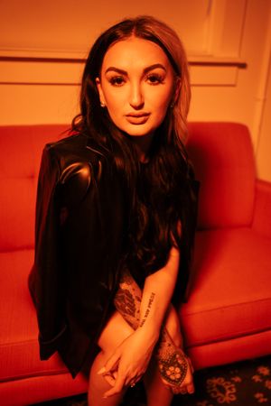Stylized portrait with warm orange lighting and black clothing against red background.