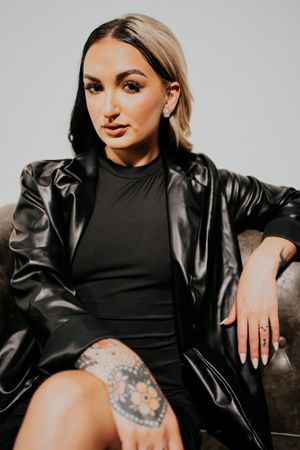 Stylish portrait with leather jacket and black dress against gray background.
