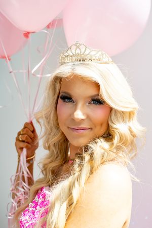 Festive portrait with tiara against pink balloon background.