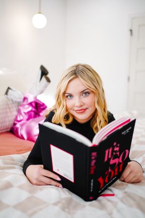 Lifestyle photo of person reading black book while relaxing on white bedding.