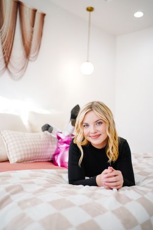 Casual portrait on white bedding showing relaxed pose in bright bedroom setting.